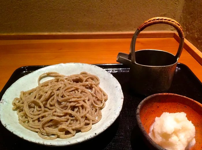 A serving of soba accompanied by a pitcher and a side dish of yuba.