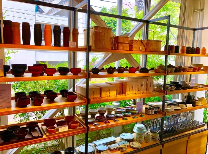 A colorful display of cookware in front of expansive floor-to-ceiling windows that reveal a lush, sunlit landscape outside.