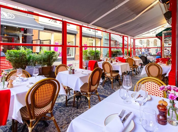 A spacious covered terrace adorned with cane chairs and elegant white tablecloths.