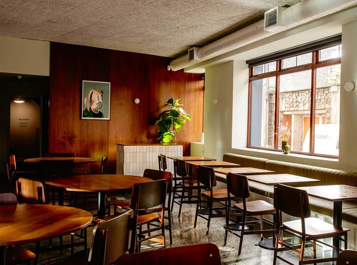 A stylish restaurant interior featuring abundant wood accents and large windows.