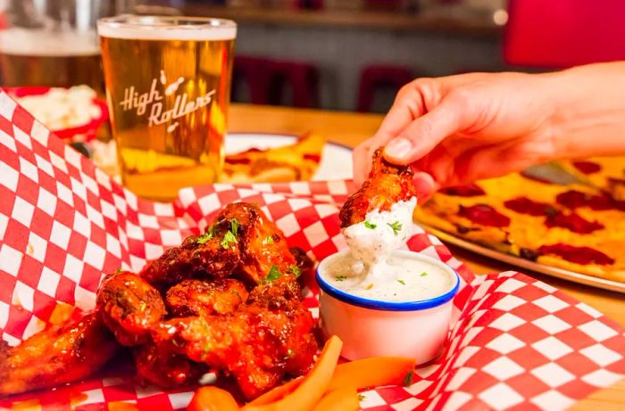 A hand dips a chicken wing into sauce.