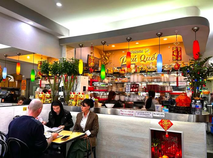 A group of diners enjoying their meal in front of a vibrant kitchen adorned with multicolored pendant lights.