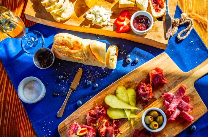 An overhead view of a chaotic table featuring an array of charcuterie, cheeses, breads, fruits, and wine.