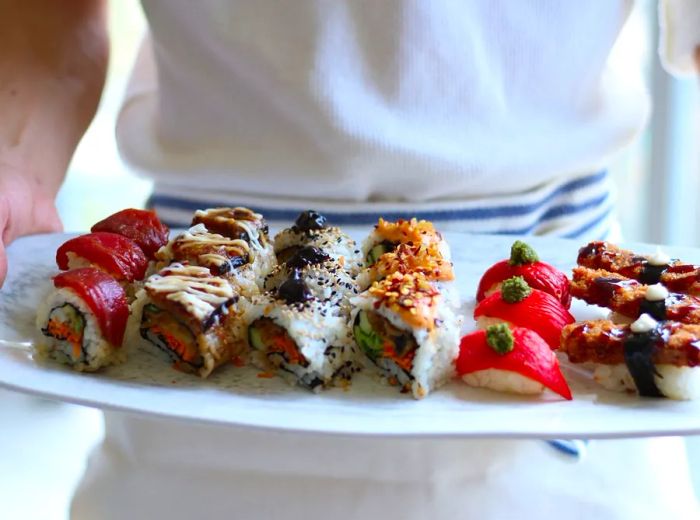 A staff member presents a platter of sushi rolls.