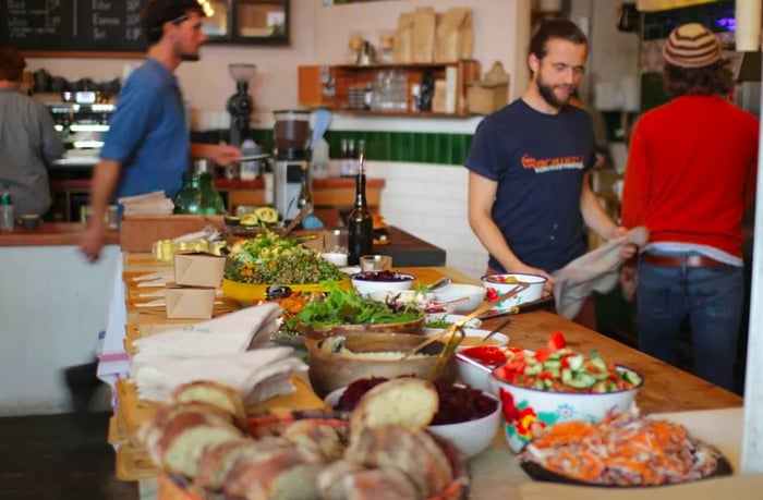 A long wooden table displays a buffet while guests mingle nearby.