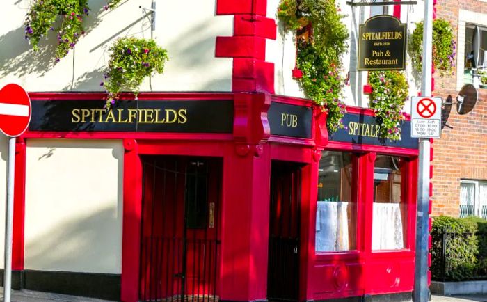 The restaurant features a crisp white exterior accentuated by bold red trim around its entrance, showcasing the names ‘Spitalfields’ and ‘pub’.