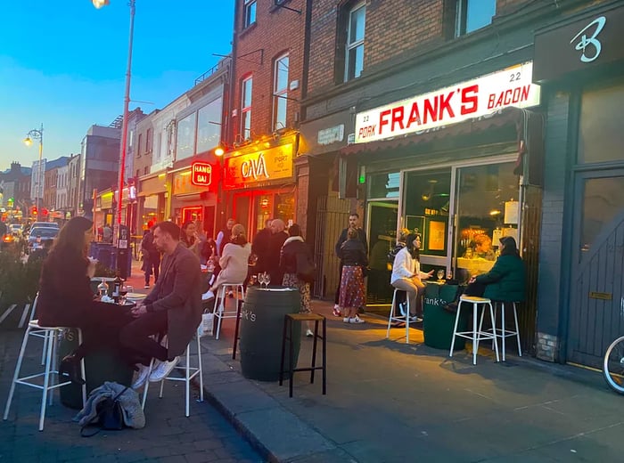 Patrons enjoying their meals on the sidewalk outside a red-brick restaurant prominently featuring a large sign that reads Frank’s.