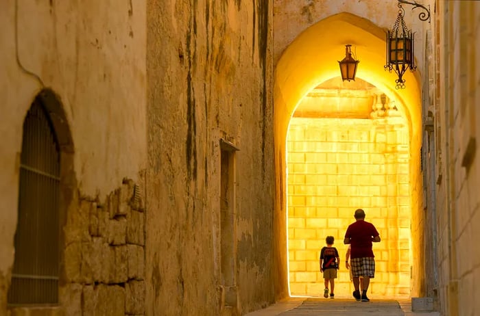 Shadows of individuals strolling through the historic streets of Mdina, Malta.