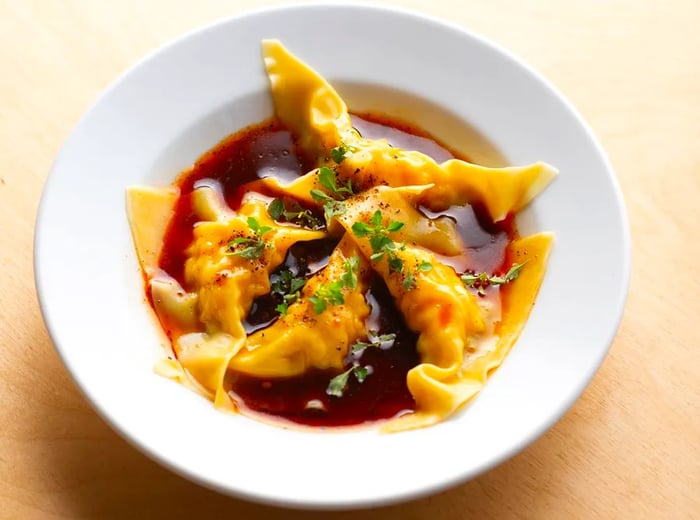 A bowl filled with dumplings immersed in rich chile sauce, garnished with tiny green sprigs.