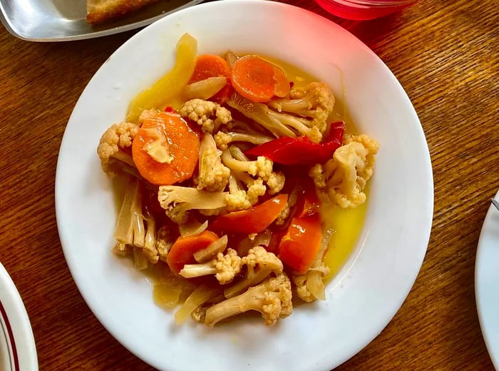 A bowl filled with cauliflower, carrots, and various other vegetables swimming in a golden broth.