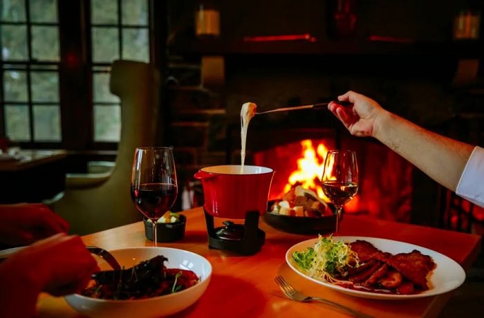 A hand dips a piece of bread into a fondue pot, allowing the excess cheese to drip off.