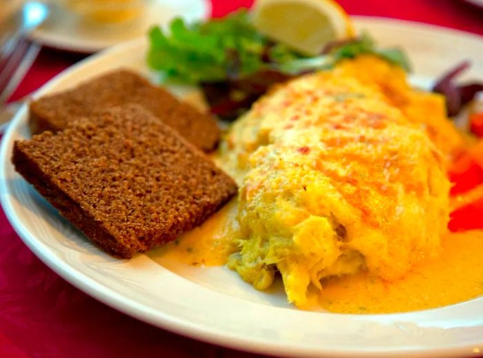 A dish featuring a generous portion of hashed fish accompanied by two slices of rye bread and a small side salad.