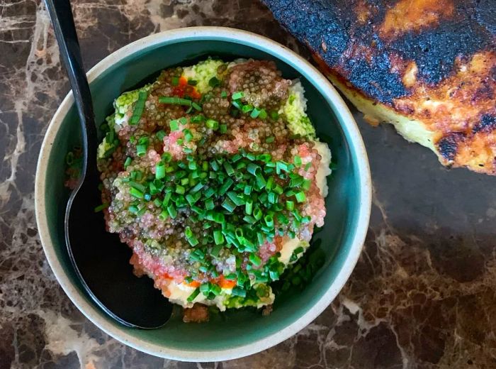 A small dish featuring lumpfish roe and ricotta topped with chives, accompanied by a large piece of charred flatbread.