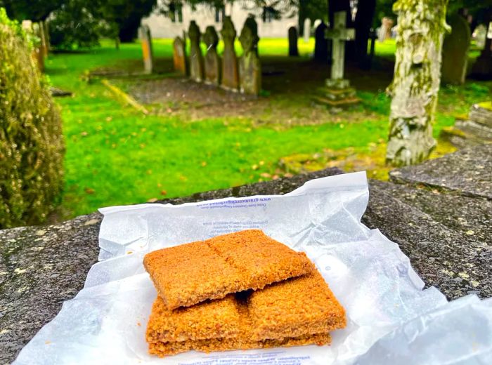 A small stack of gingerbread rests atop a stone wall, with a graveyard visible in the background.