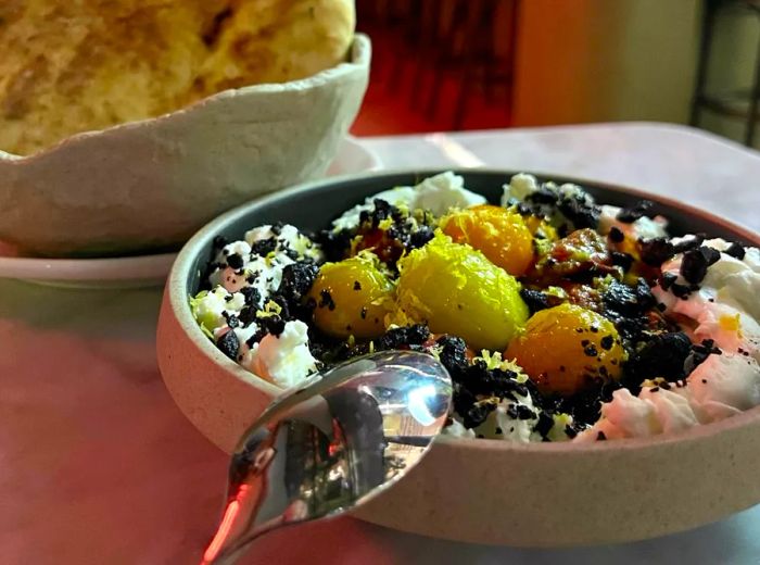 A plate featuring vibrant chunks of yellow and orange atop fluffy white labneh, accompanied by pita bread.