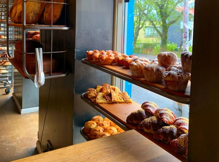 Delicious pastries displayed on shelves in front of a window, alongside caged shelving filled with loaves of bread.