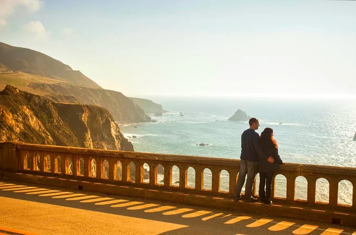 A couple gazing over the breathtaking view from Bixby Bridge along Highway 1, near the rugged Big Sur coastline of the Pacific Ocean in California, USA