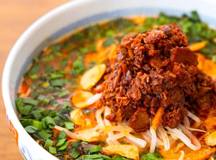 A soup bowl adorned with herbs, nuts, and a generous scoop of brown meat paste.