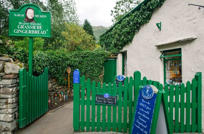 The façade of a quaint, stucco-sided cottage, complete with a green picket fence and large signs advertising Grasmere Gingerbread.