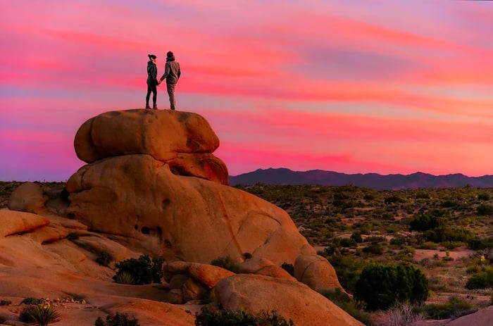 A couple standing on a rock at sunset in Joshua Tree National Park, California, USA