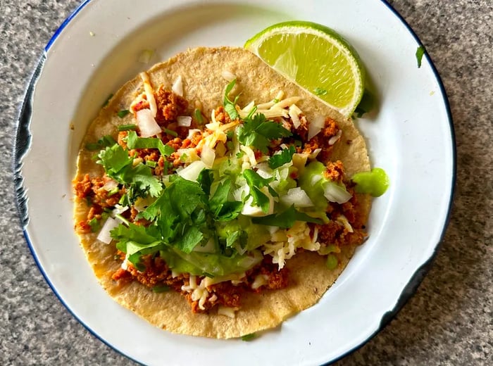 A sizable taco dominating an enamel plate, lavishly topped with chopped cilantro and served with a lime wedge.