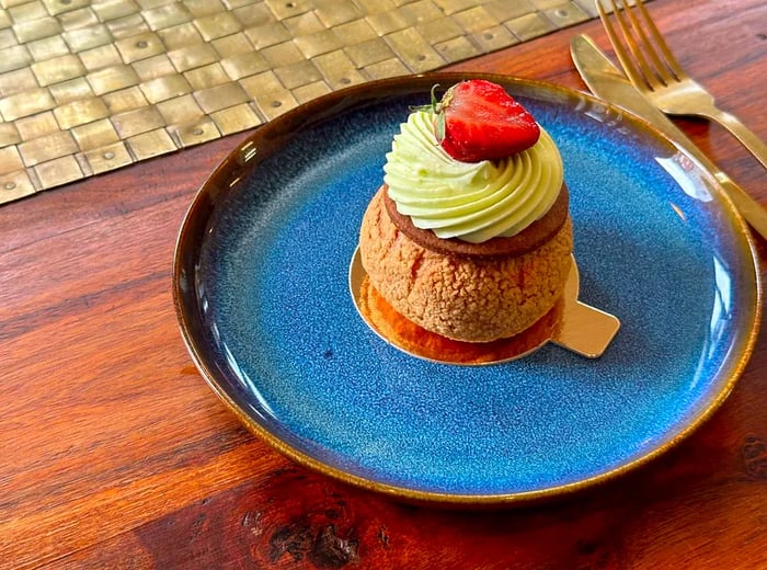 A choux pastry adorned with a swirl of icing and topped with half a strawberry.