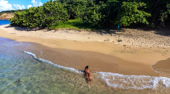 A woman relaxes on her stomach on the sands of Point Baptiste Beach as the waves gently wash over her, Dominica