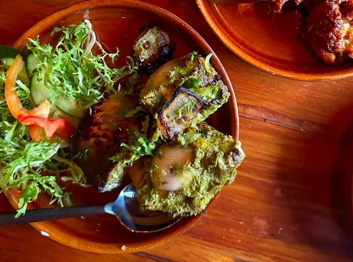 On a wooden table sit two dishes, one featuring chunks of salmon atop a bed of greens.