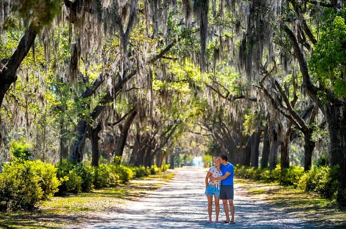 A man kisses a woman’s cheek on a pathway bordered by Spanish moss trees in Savannah, Georgia, USA