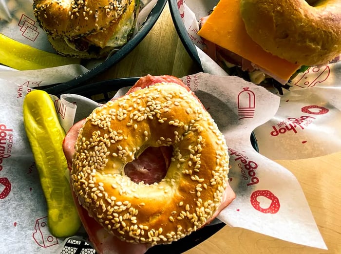 A close-up of bagels adorned with fillings, accompanied by pickles on the side.