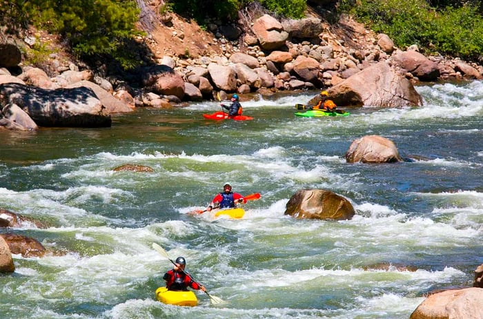 People in small kayaks paddle down a river