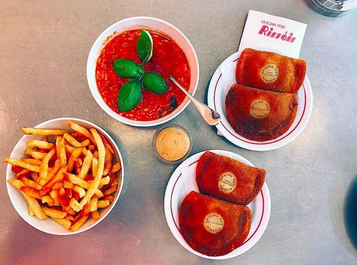 Two plates filled with turnovers accompanied by a bowl of crispy fries and a bowl of savory tomato rice.