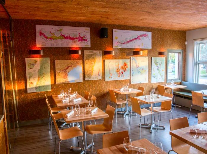 An afternoon view of a bright dining area featuring light wood tables, sleek chairs, and maps adorning a textured wall.