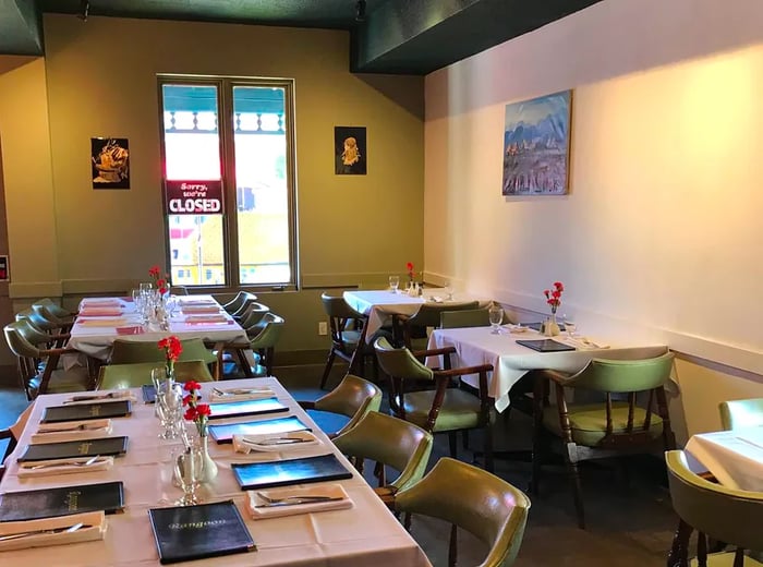 An interior view of a restaurant featuring tables prepared for lunch, complete with menus and bright, sunlit windows at the back.