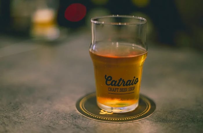 A beer resting on a coaster atop a concrete surface, with the name Catraio elegantly stenciled on the glass.