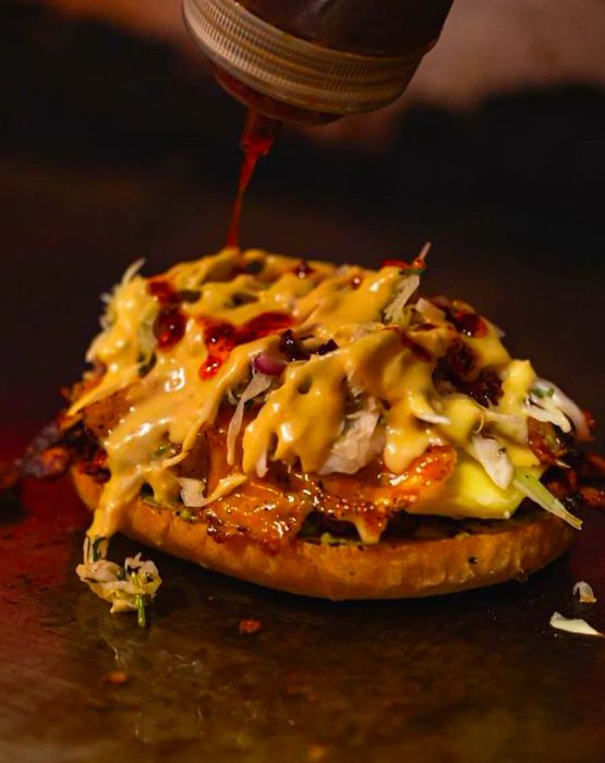 A chef decorates a generously piled open sandwich with a drizzle of sauce.