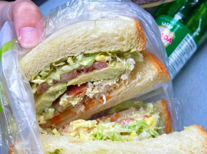 A sandwich loaded with meats and vegetables, cut in half to reveal its fillings.