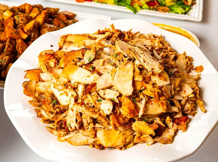 A serving of chicken shawarma, accompanied by various platters of food.