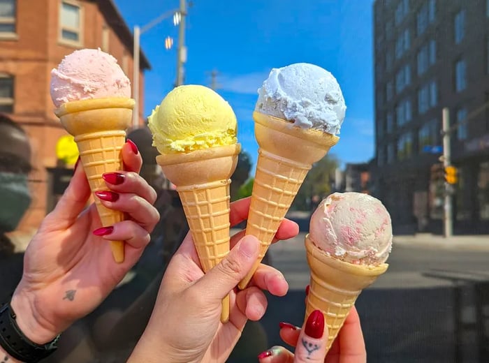 A pair of hands showcases four vibrantly colored ice cream cones against a clear day backdrop on a busy street.