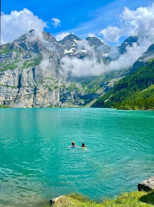 Two women enjoy swimming in turquoise waters, framed by towering snow-capped mountains.