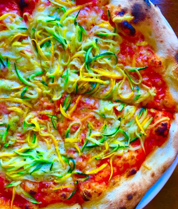 A close-up of a pizza adorned with vibrant yellow and green shaved zucchini.