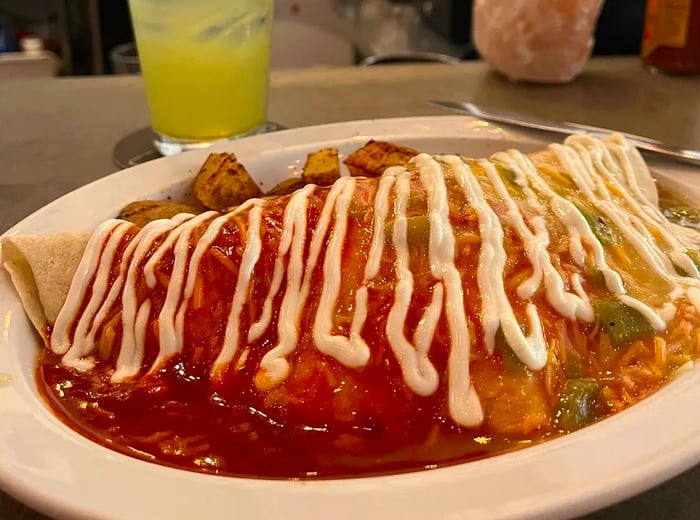 A close-up of a quesadilla drizzled with white sauce, accompanied by a margarita in the background.