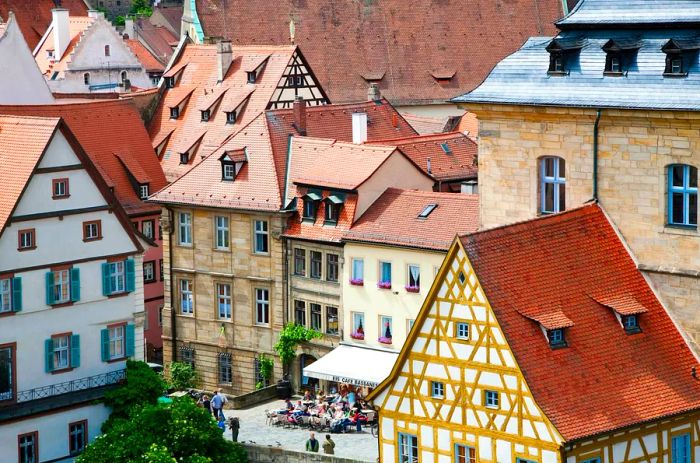 Red-tiled roofs slope down to a lively square where patrons enjoy drinks at an outdoor café.