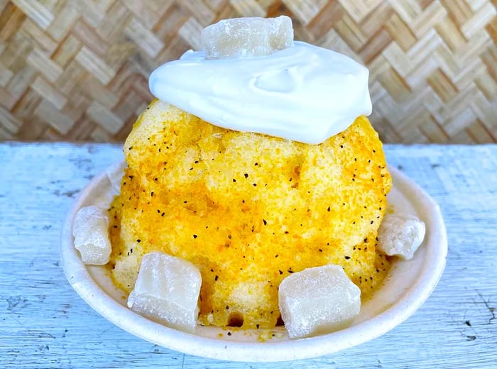 A vibrant yellow mound of shave ice, generously topped with whipped cream and accompanied by cubes of mochi.