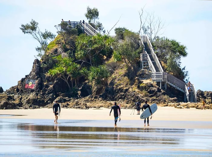 A wide-angle shot of surfers carrying their boards at the renowned surfing destination, The Pass, Byron Bay, NSW