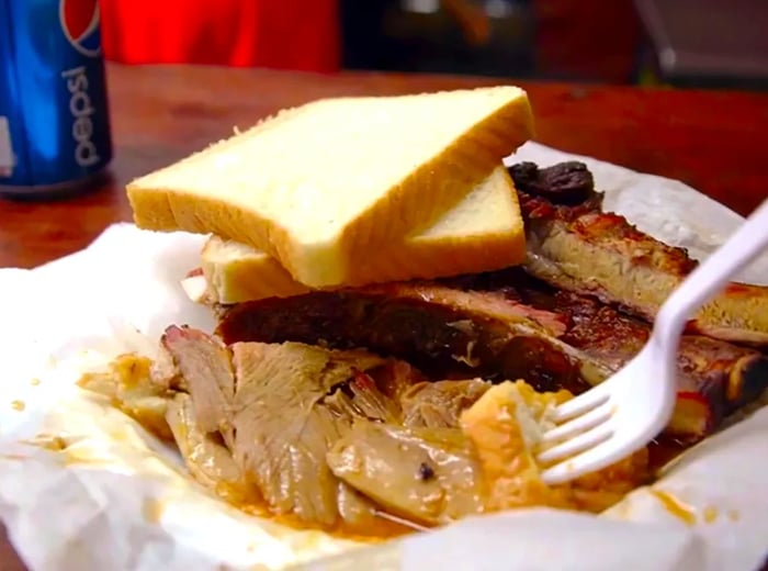 Ribs and assorted meats served on wax paper alongside slices of white bread.