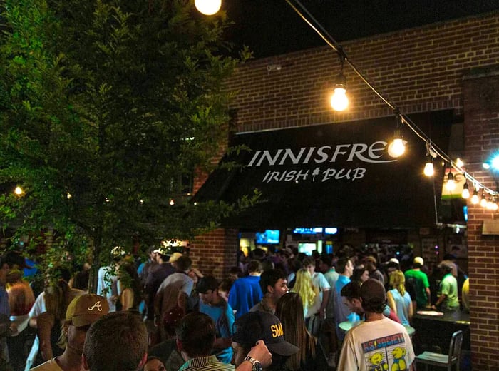 A lively group of young patrons enjoying the patio at a redbrick pub, with an awning that reads Innisfree Irish Pub.