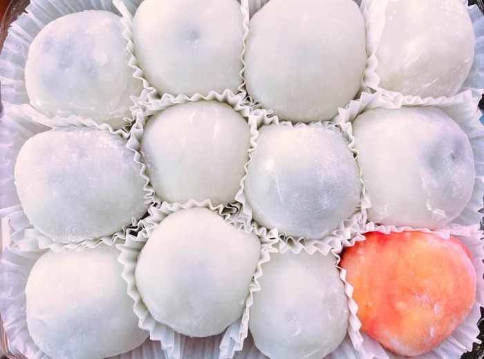 A dozen pieces of mochi, all white except for one red piece in the corner, neatly arranged in paper cups.