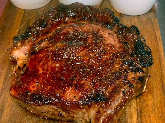 A sizable steak displayed on a cutting board accompanied by three sauces in ramekins.