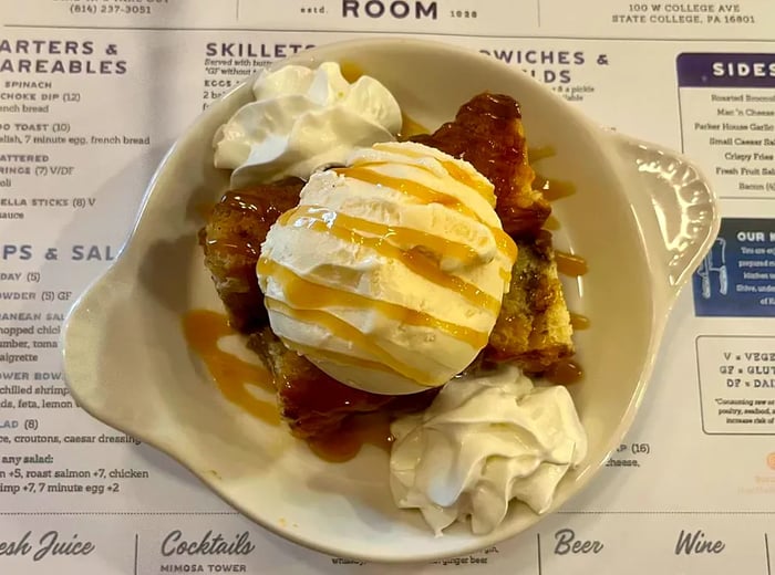 A generous scoop of vanilla ice cream atop grilled stickies, drizzled with caramel sauce, presented on a white dish over a restaurant menu.